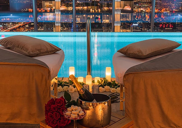 Two massage tables by an infinity pool with candles and flowers at night.