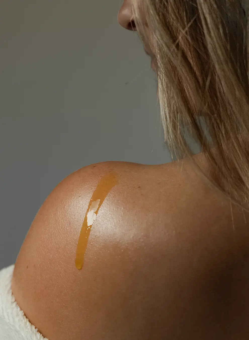 Close-up of a person's shoulder with a golden oil applied to it against a neutral background