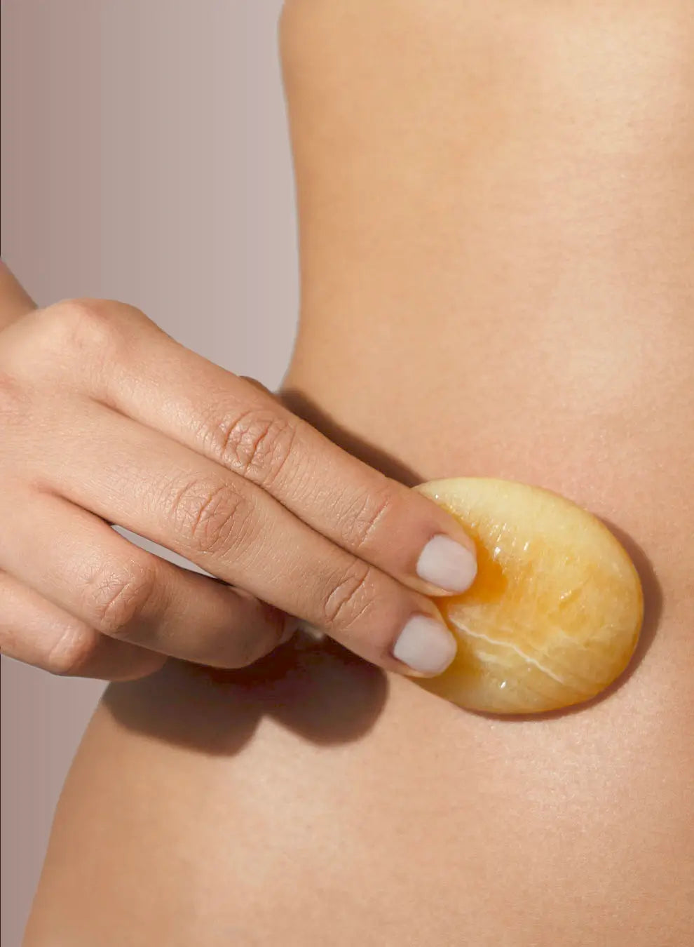 Hand applying a yellow gemstone to a person's skin on a neutral background