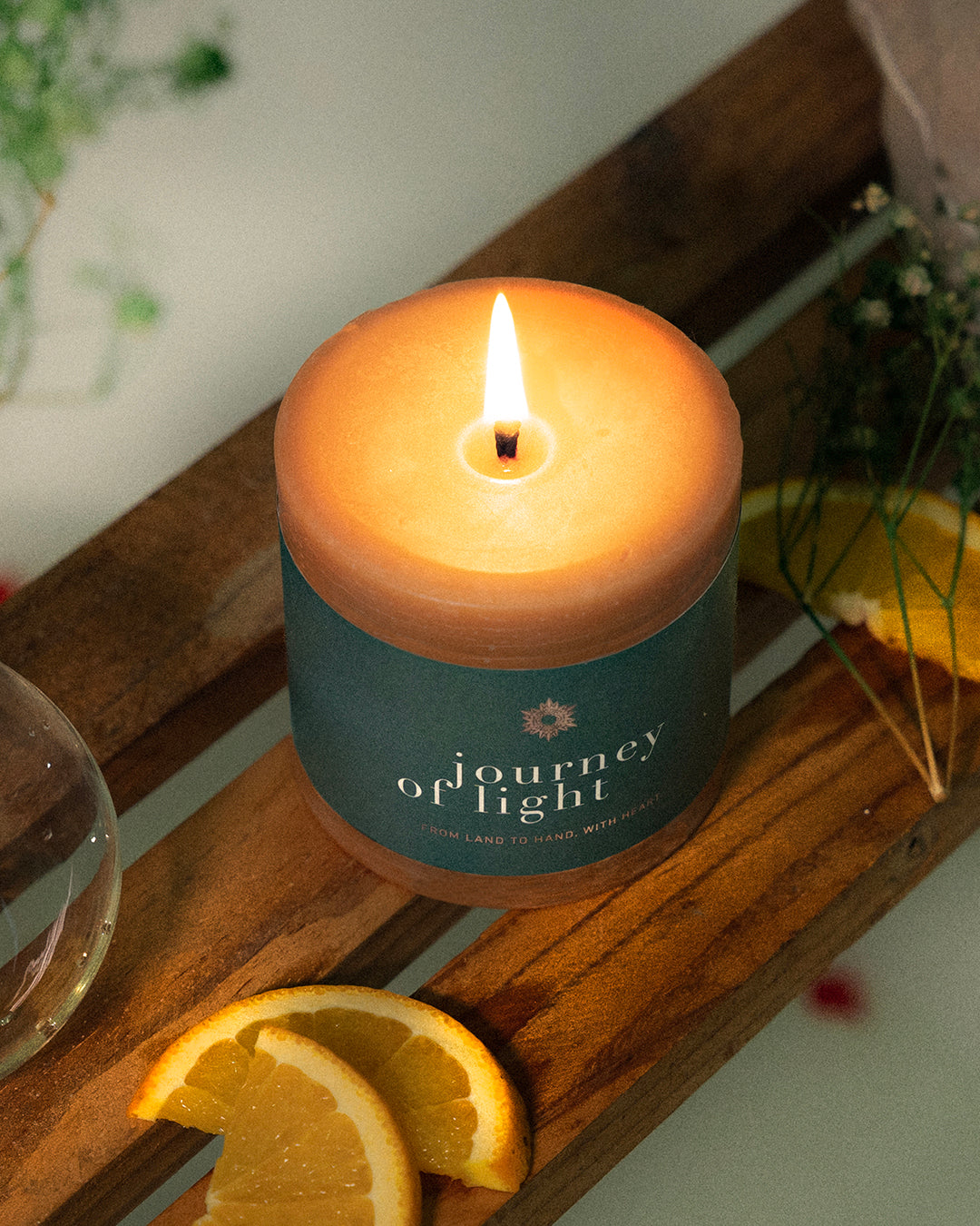 Candle labeled 'Journey of Light' on a wooden surface with oranges and cinnamon sticks.