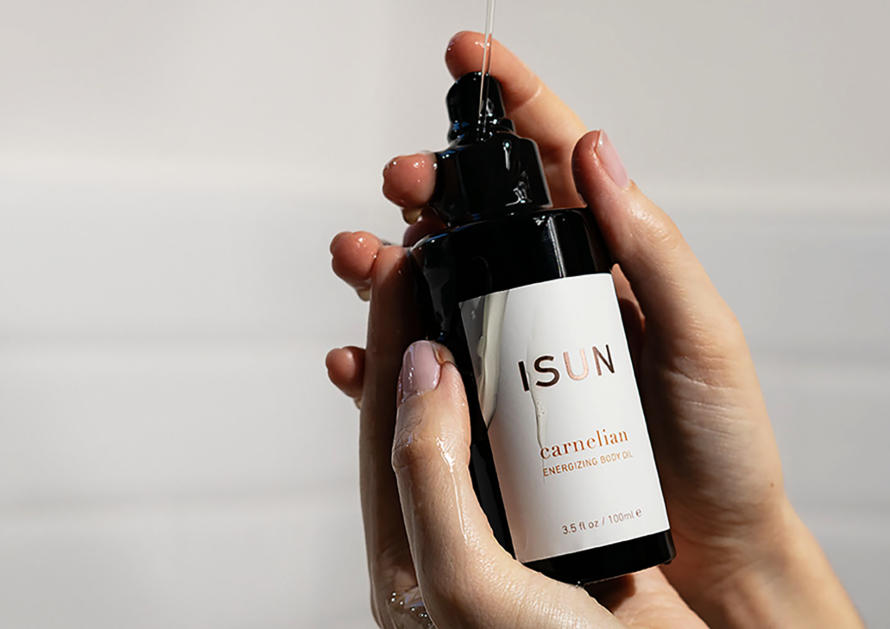 Hand holding a black skincare bottle labeled 'ISUN' against a neutral background