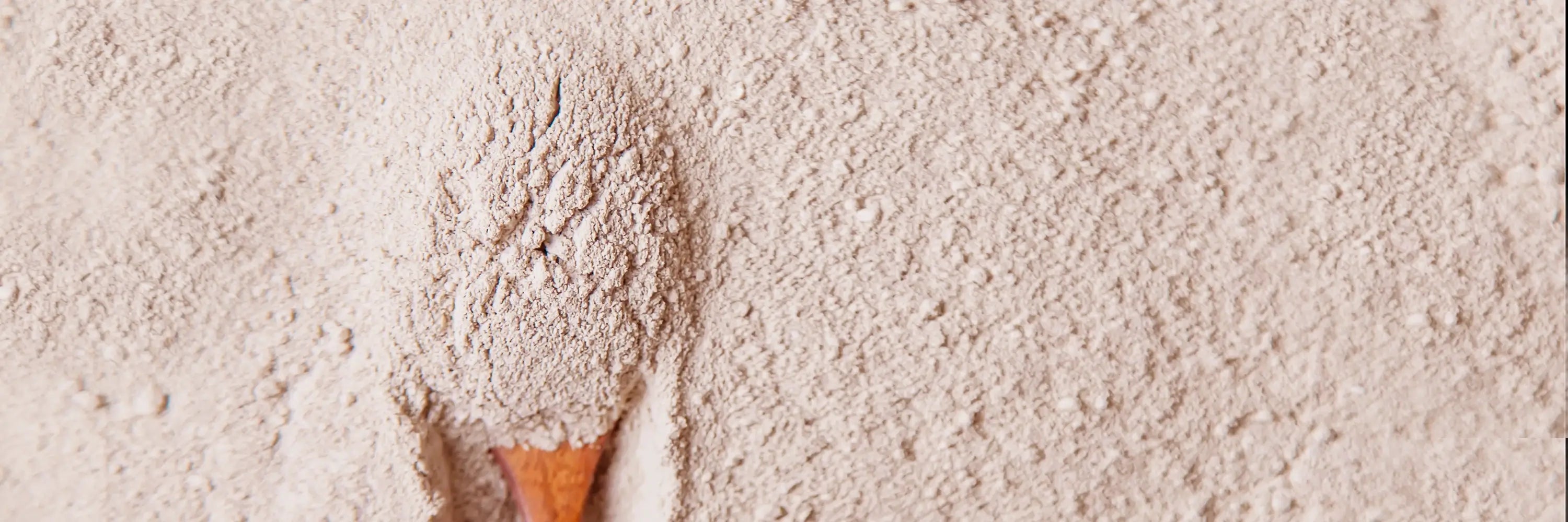 Wooden scoop filled with Rhassoul clay on a bed of clay