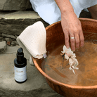 Person dipping a flower into a copper basin with a bottle of ISUN skincare product nearby.