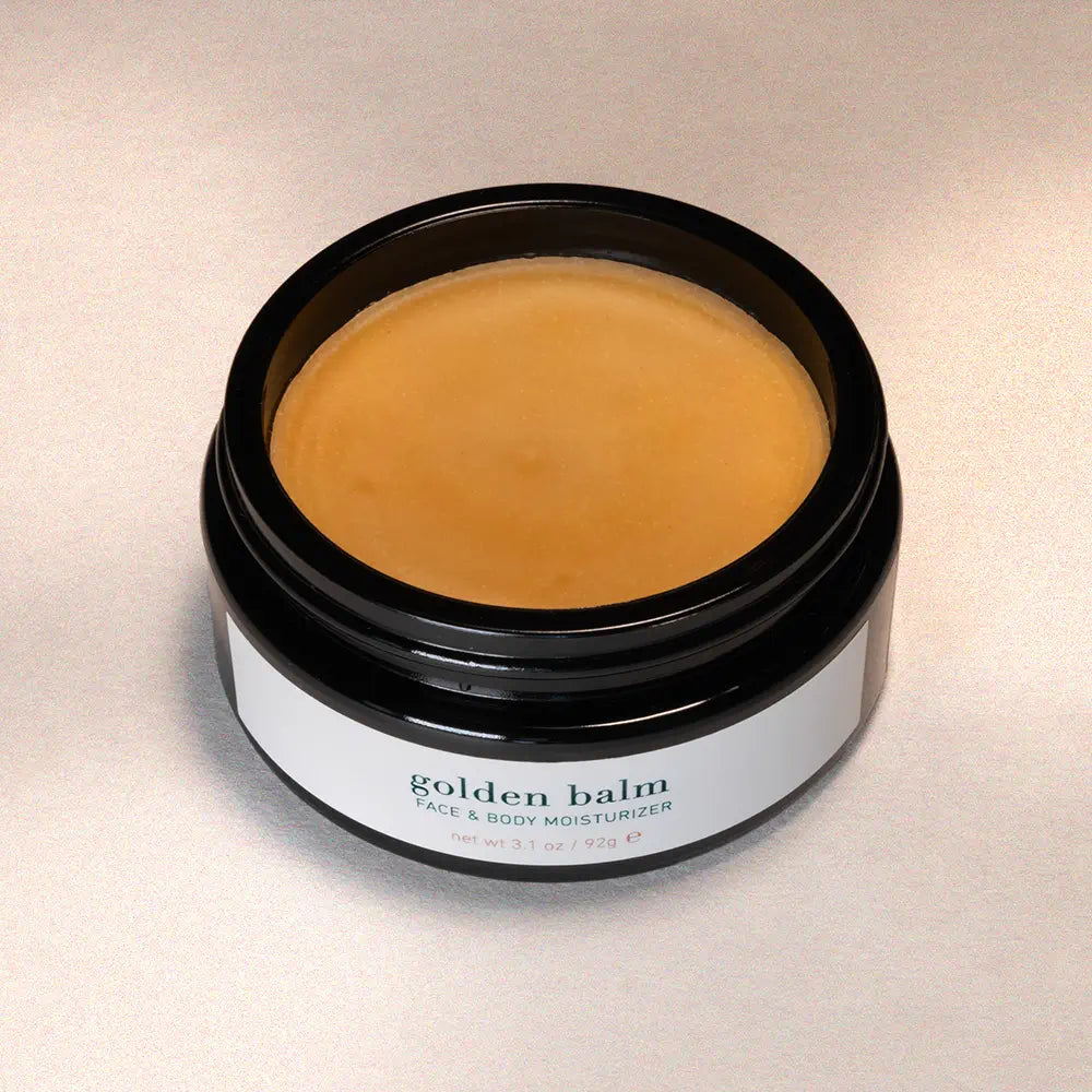 Jar of 'golden balm' face and body moisturizer on a neutral background
