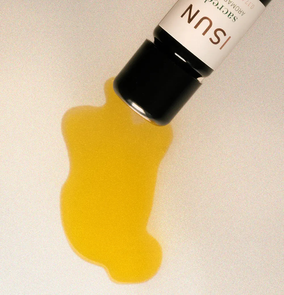 Yellow liquid spilling from a bottle labeled Sacred on a beige background