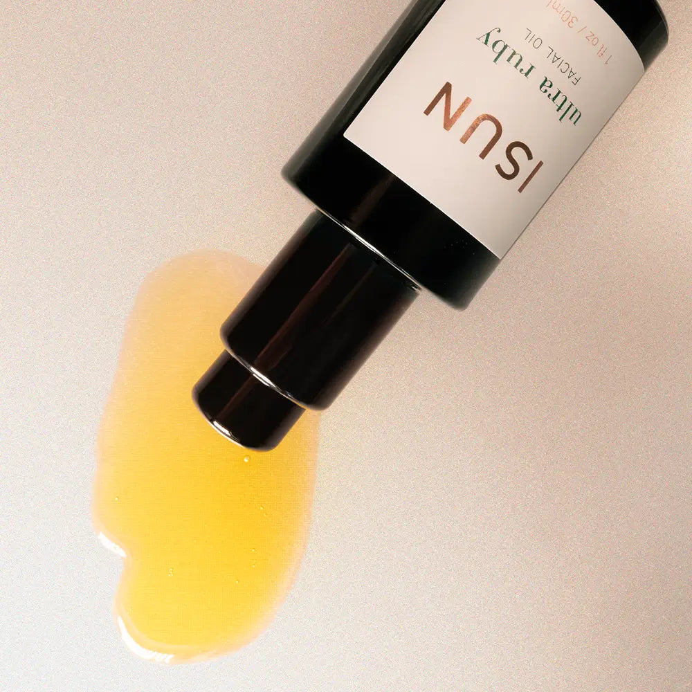 Bottle of ISUN skincare product with a droplet of yellow liquid on a beige background