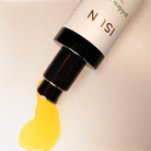 Cosmetic product with golden oil being squeezed out on a beige background