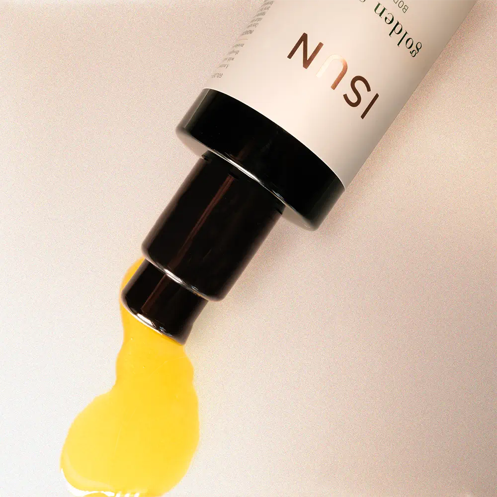Cosmetic product with golden oil being squeezed out on a beige background