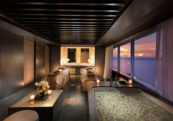 Modern spa room with a bathtub, candles, and a view of the ocean.