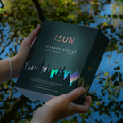 Hands holding an ISUN Restore Ritual gift box beside water reflecting green foliage.